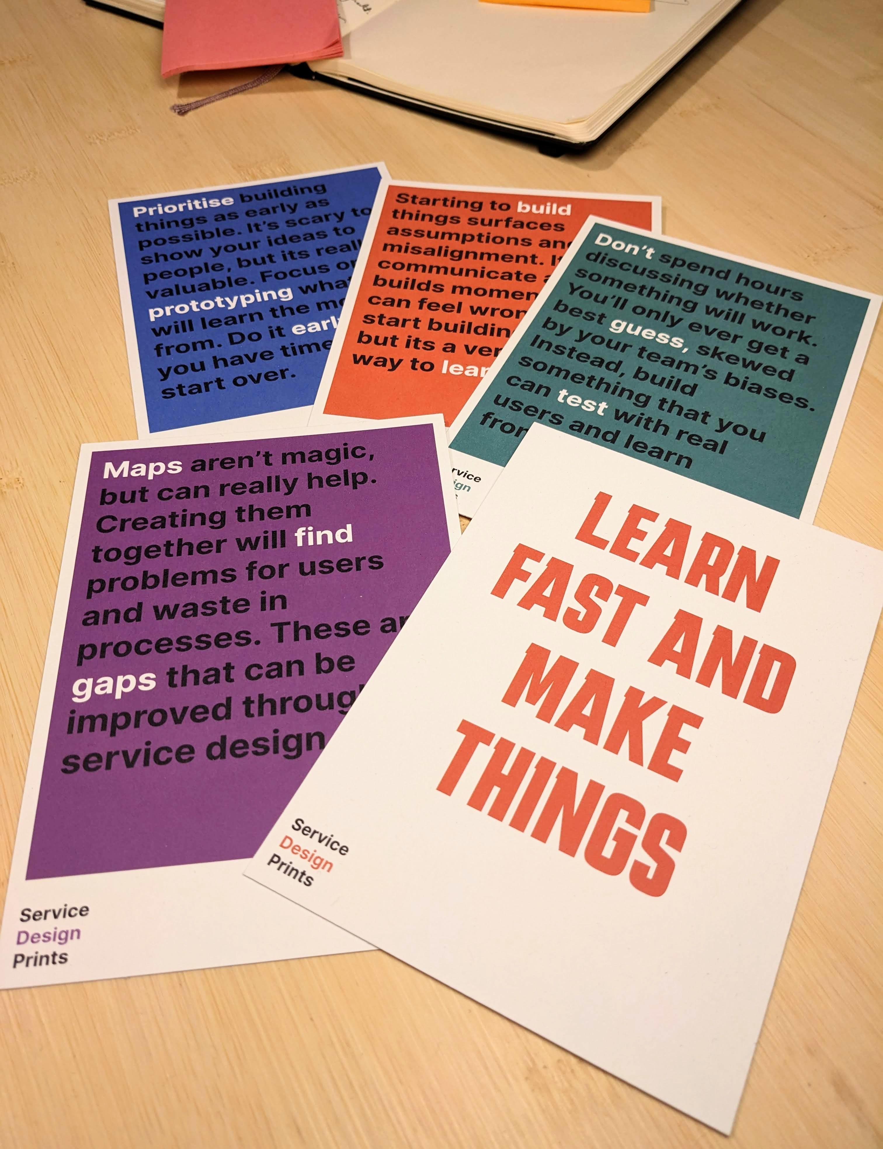 Postcards on a desk. The top one says 'Learn fast and make things' in red text on white background.